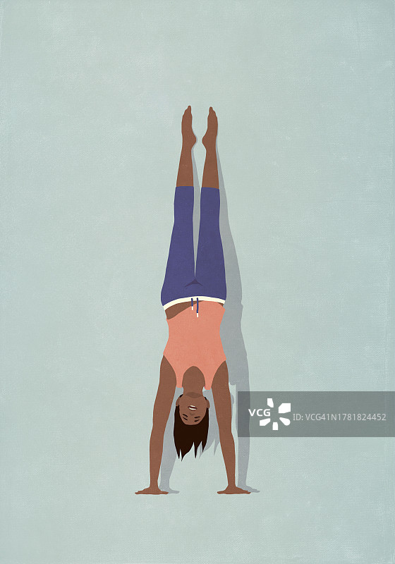 健康女人在蓝色背景上练习瑜伽手倒立图片素材