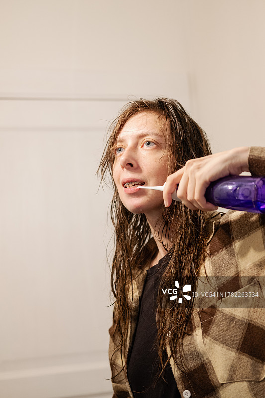 在浴室里用冲牙器在镜子前刷牙的年轻女人图片素材