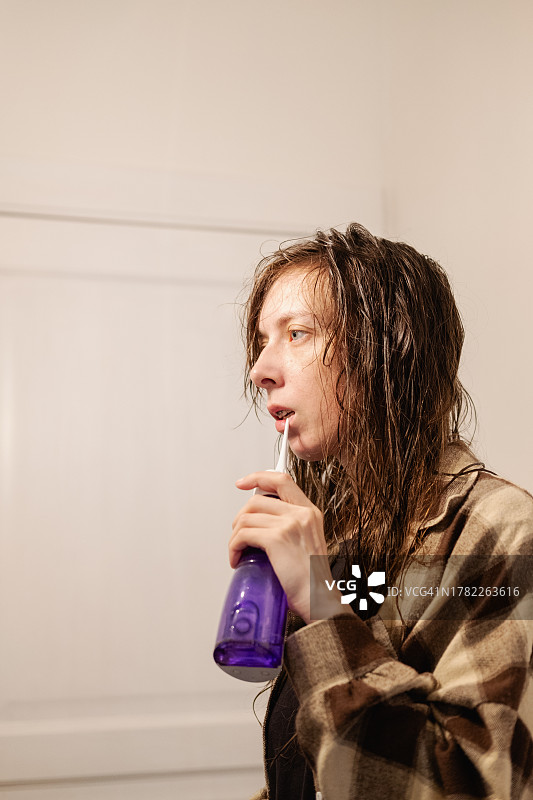 在浴室里用冲牙器在镜子前刷牙的年轻女人图片素材