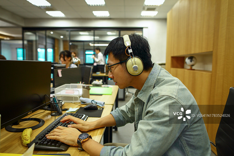 亚洲男白领戴着头戴式耳机认真工作图片素材