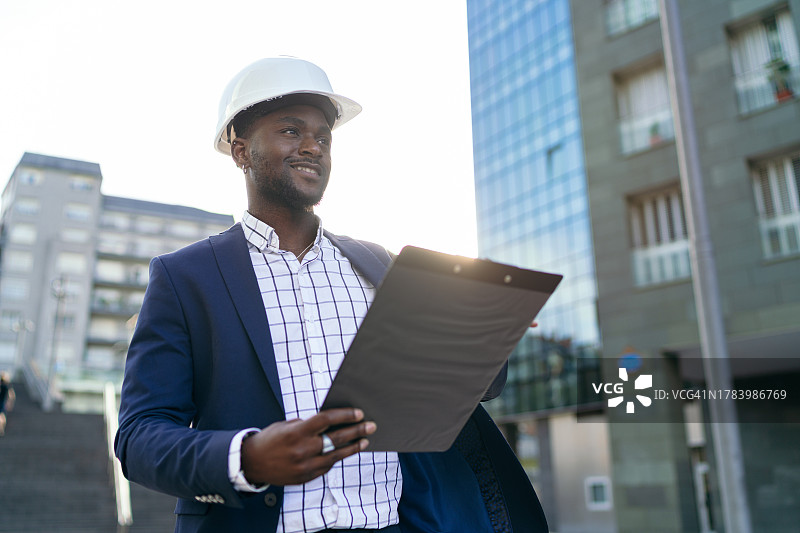 在城市建筑工地拿着剪贴板的自信非洲工程师图片素材