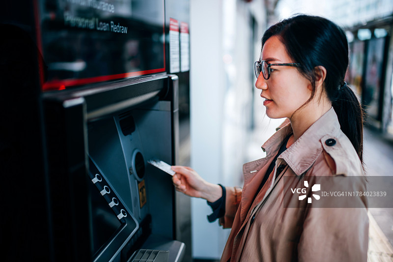 年轻的亚洲女性在城市街道的自动取款机上插入银行卡取款图片素材