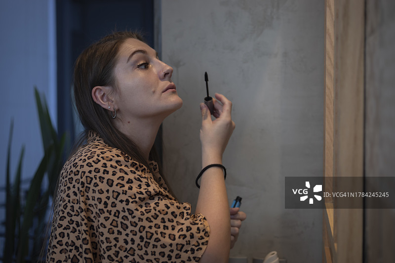 年轻的白人女子在家中浴室镜子前准备时，在眉毛上涂睫毛膏图片素材