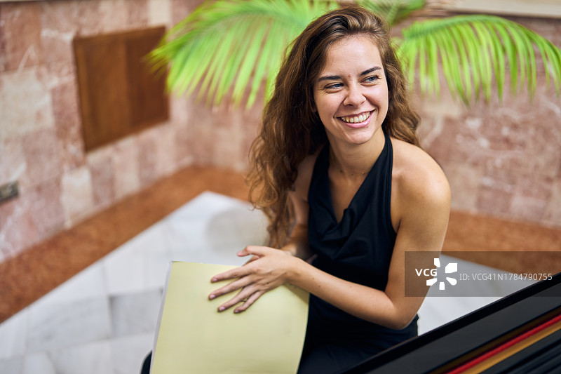 坐在钢琴旁拿着音乐笔记本的微笑女人图片素材