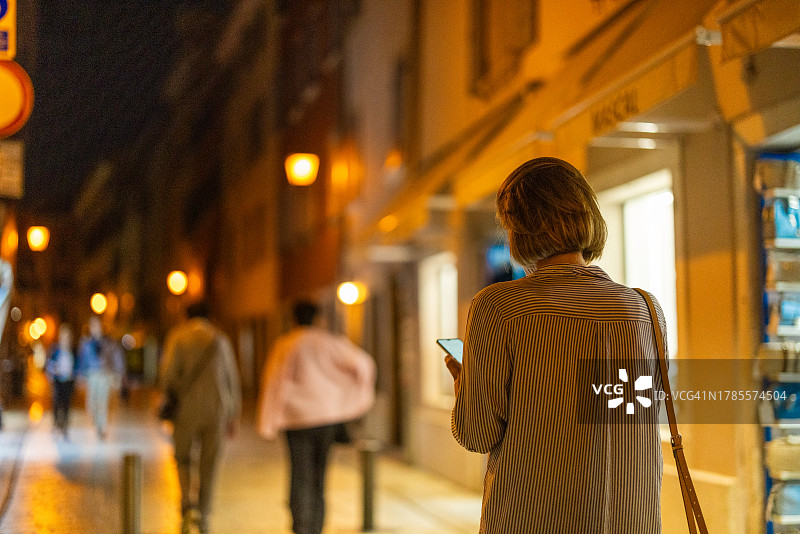 夜晚在街上使用手机APP叫出租车的女人。夜晚看手机的女人。图片素材