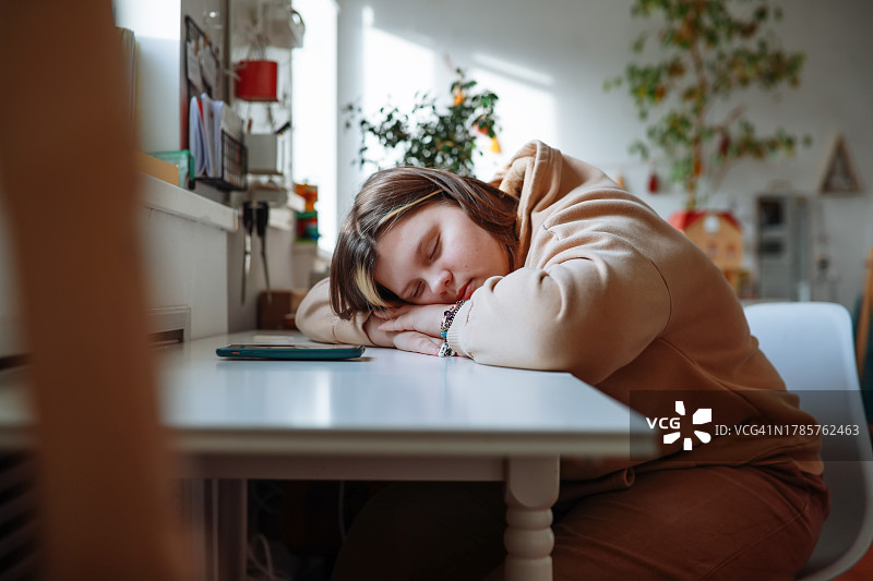 疲惫的超重青少年在家中小憩，桌上有智能手机图片素材