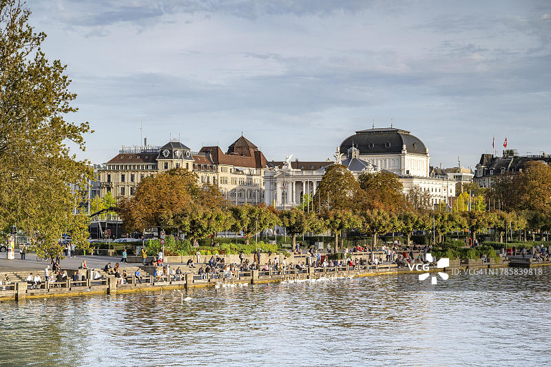 人们坐在苏黎世湖岸边的码头上，背景是歌剧院，瑞士苏黎世州图片素材