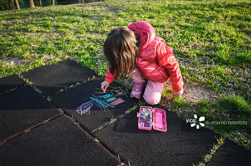 在公园的人行道上用粉笔画画的小女孩图片素材