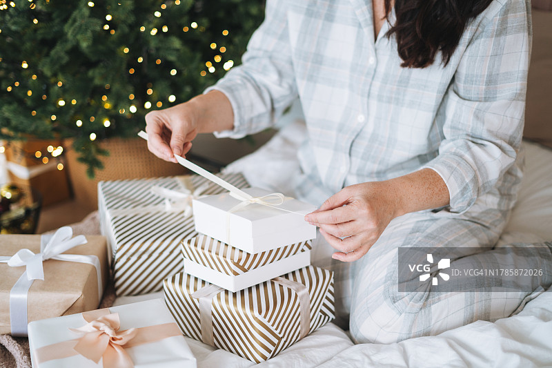 圣诞节早晨，穿着家居服的棕发女人在家里的床上包装礼物图片素材