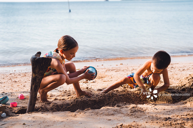 男孩和女孩在海滩上兴高采烈地挖沙子和大坑图片素材