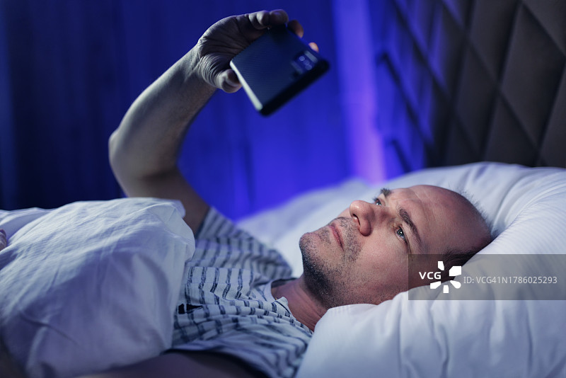 中年谢顶男子躺在床上使用手机图片素材