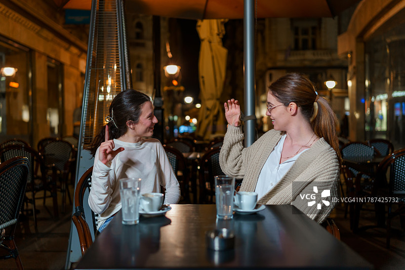 两位女性朋友在风景如画的咖啡馆花园里用手语分享秘密图片素材