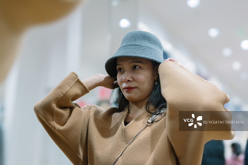 亚洲女子在商场挑选冬季帽子图片素材