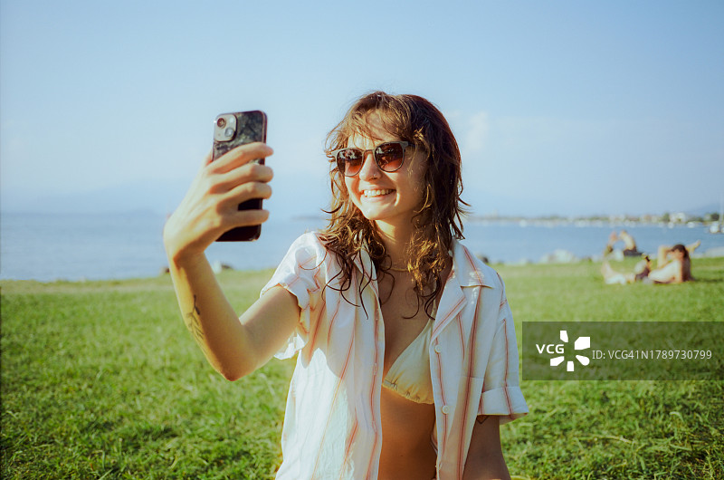 在加尔达湖附近度假时用智能手机自拍或进行视频通话的女人图片素材