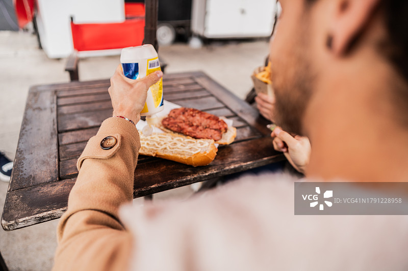 在餐车上吃香肠面包的男人：涂抹蛋黄酱图片素材