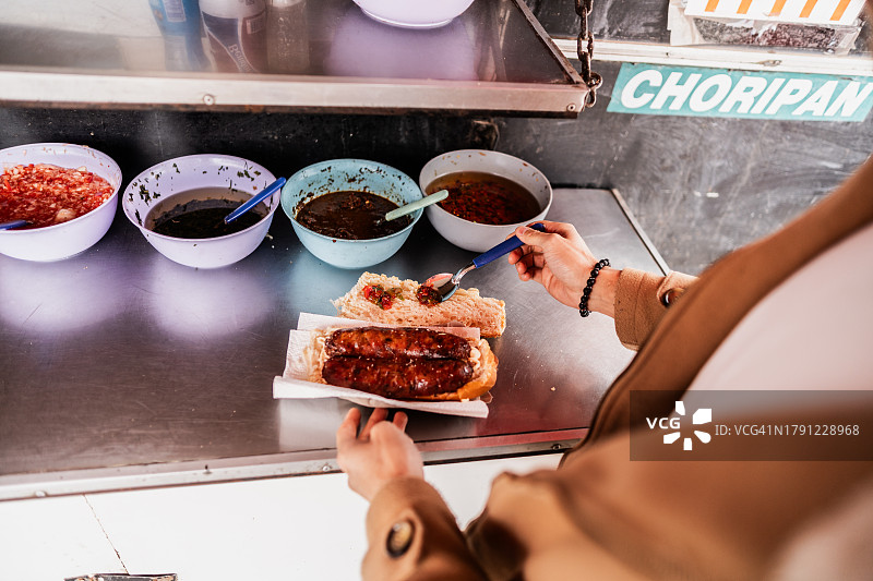 男子在餐车上吃阿根廷香肠面包并淋上油醋汁的特写图片素材