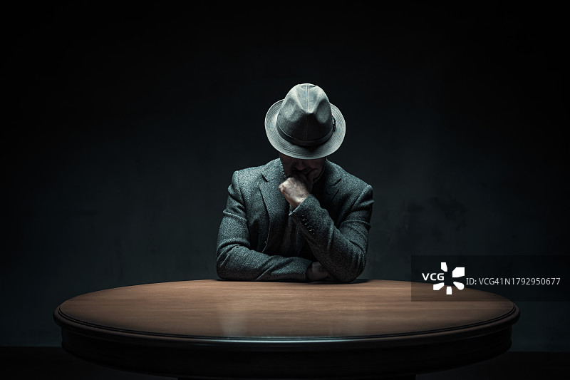 在黑暗房间里手托下巴坐在桌旁的神秘的沉思的男人图片素材