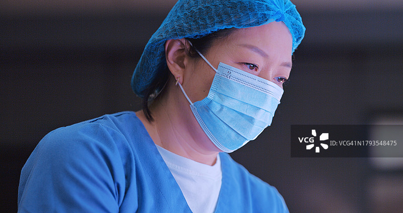 戴着个人防护装备的外科医生，在手术室思考和工作的医护女性。在ICU暗室里解决问题和进行紧急医疗保健的医生或护士图片素材