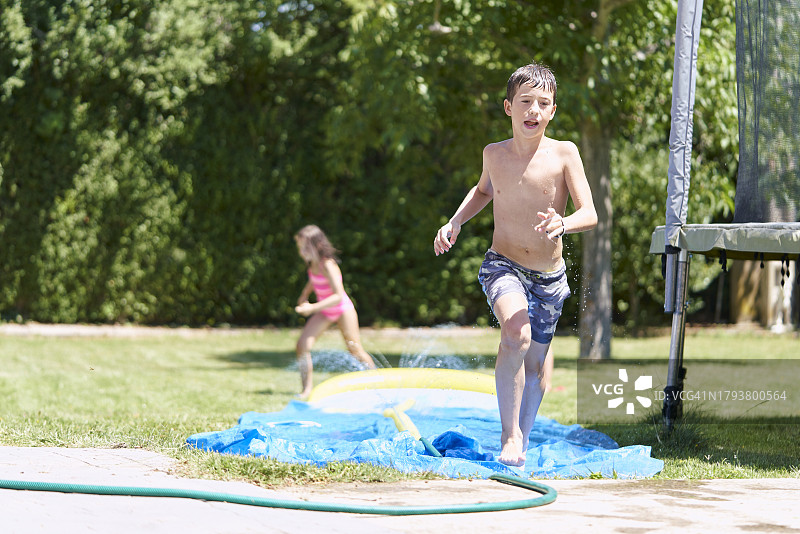 姐弟在花园水滑梯上奔跑的正面视角图片素材
