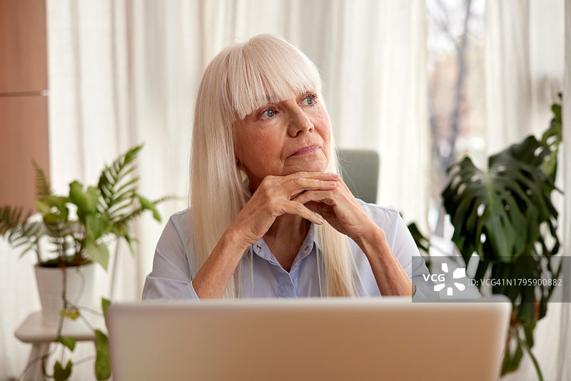 老年妇女坐着使用笔记本电脑，若有所思地望向远方图片素材