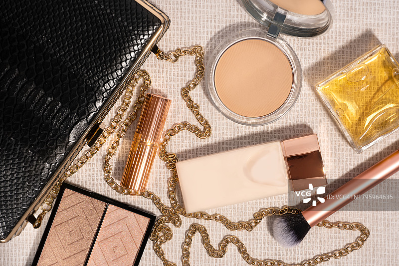 米色背景上的女士黑色手拿包和化妆品图片素材