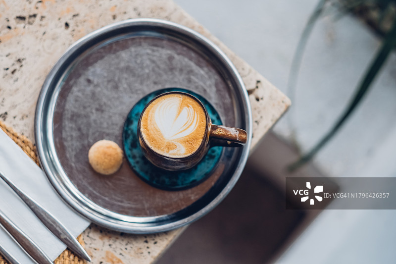金属托盘上的拉花卡布奇诺咖啡，陶瓷杯中的温馨早晨图片素材