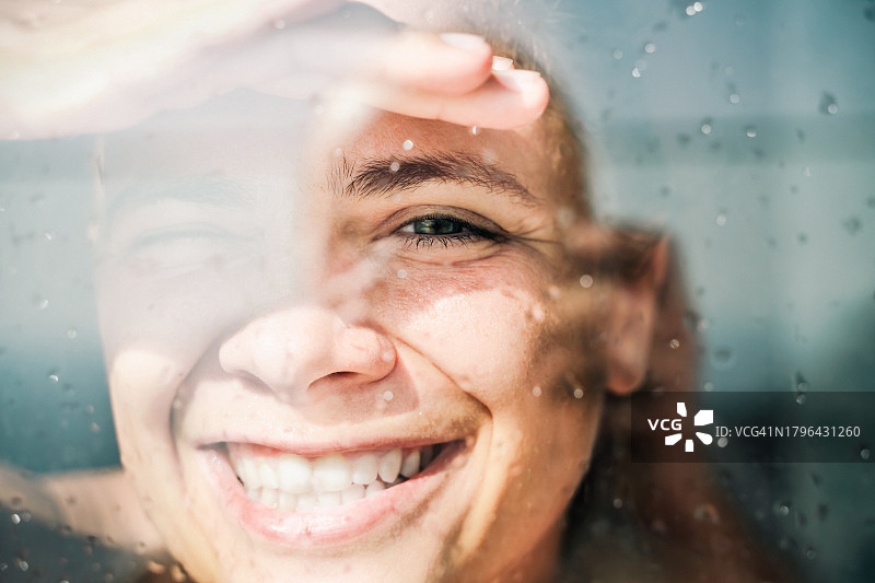 女子隔着玻璃，对着阳光微笑眯眼，特写图片素材