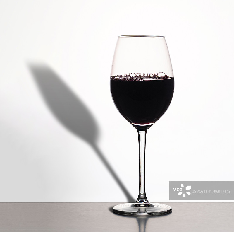 白色背景和长阴影下的桌上红酒图片素材