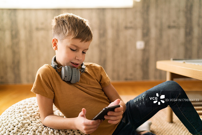 在家戴耳机玩手机的男孩图片素材