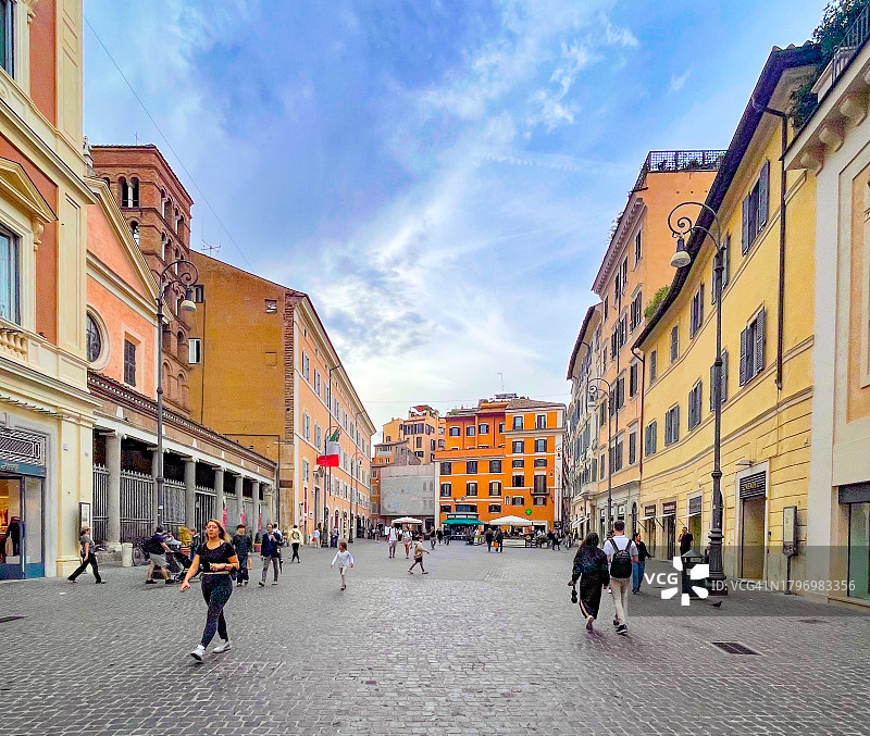 在教堂和历史建筑环绕的鹅卵石广场上行走的人们图片素材