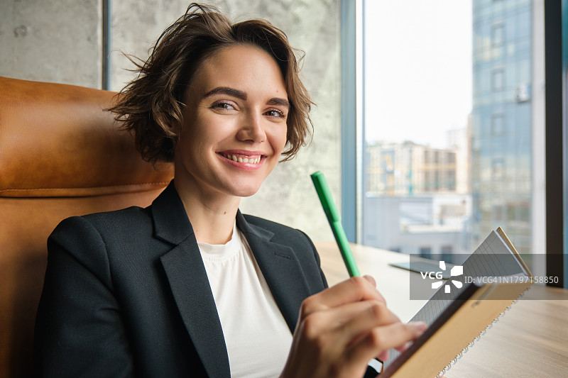 面带微笑的女商人坐在办公室里在书上写作的肖像图片素材