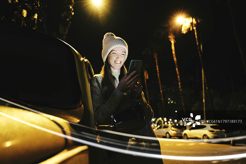节日彩灯下的购物计划：都市夜晚中快乐的智能手机用户图片素材