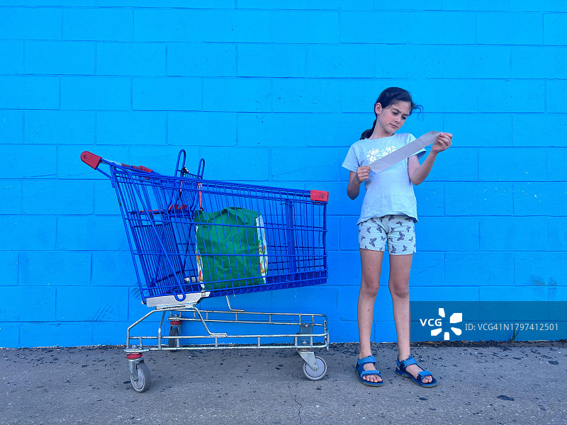 小女孩站在空购物车旁查看购物清单图片素材