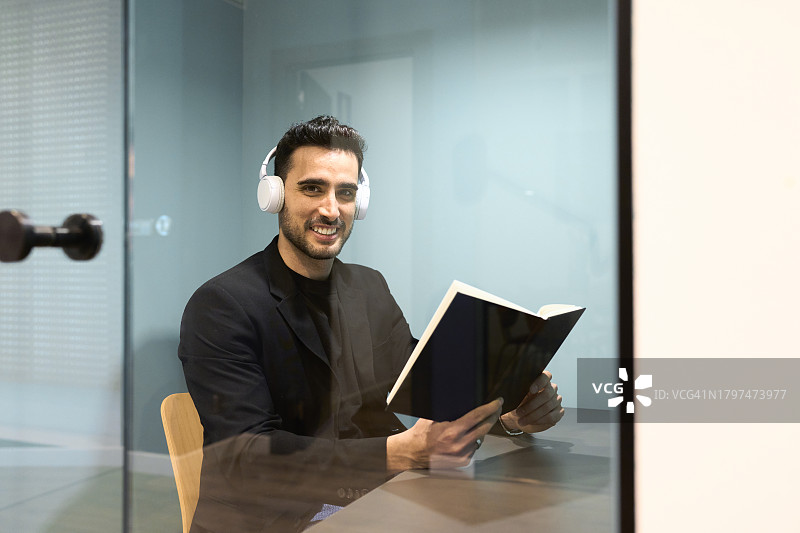 男人坐在带玻璃门的办公室隔间里看书的侧面肖像照图片素材