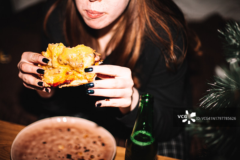 年轻女人在圣诞树旁吃自制披萨喝啤酒图片素材