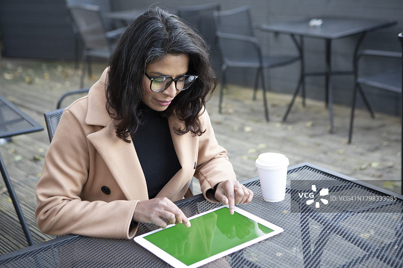 中年妇女坐在室外咖啡馆的桌旁，使用平板电脑图片素材