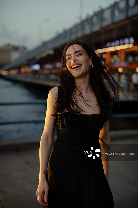 在伊斯坦布尔加拉塔桥上享受日落的微笑的年轻漂亮女人肖像图片素材
