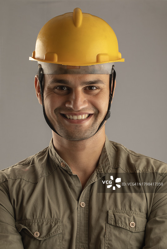 戴着安全帽站在灰色背景前的微笑男建筑师肖像图片素材