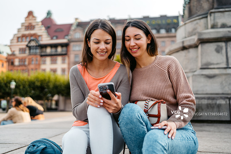 两位女性朋友瑞典马尔默大广场台阶上使用手机图片素材