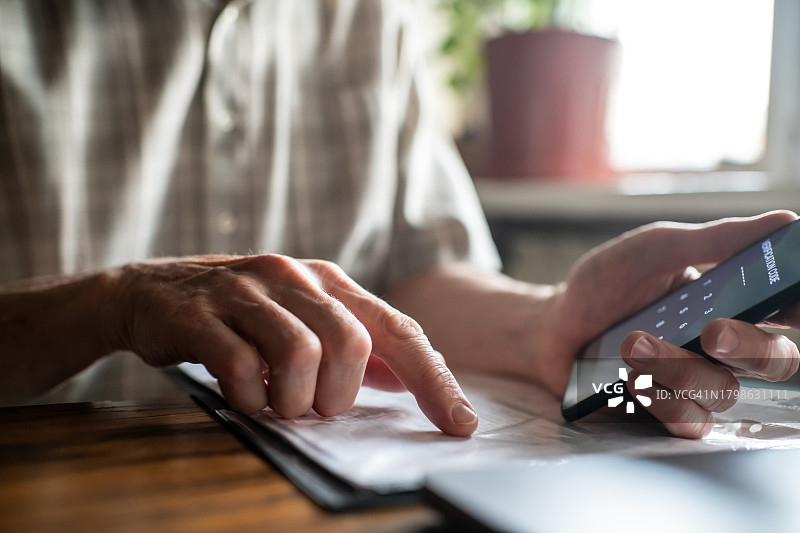 年长的男人在家中使用智能手机、笔记本电脑和账单，文件或收据输入验证码图片素材