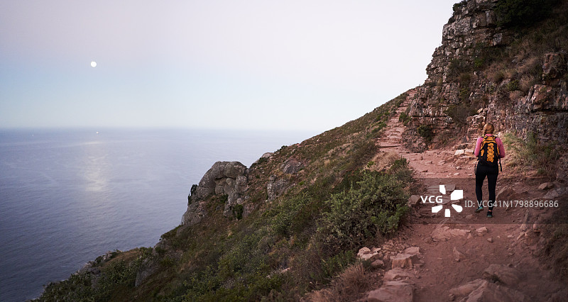 傍晚，徒步走在岩石山路上的女登山者背影图片素材