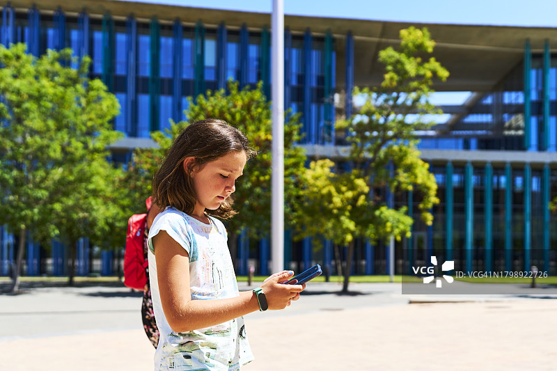 背包游客女孩站在建筑外看手机的侧视图图片素材