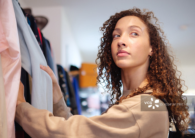 快乐的女人站在时装店里，仔细选择要购买的服装图片素材