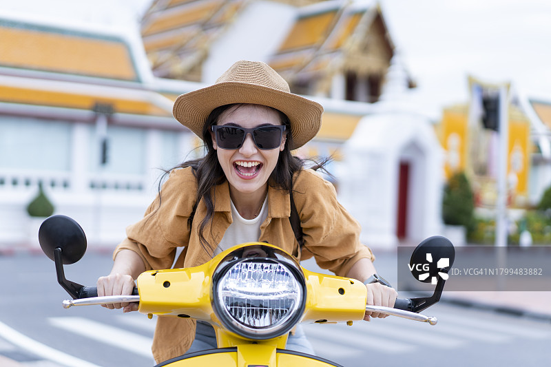 快乐的年轻女子骑着摩托车在城市街道上图片素材