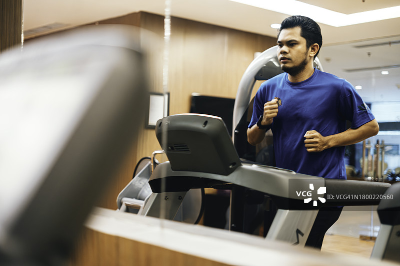 在酒店健身房跑步机上跑步的年轻亚洲男运动员图片素材