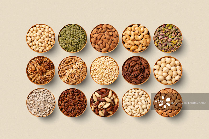 米色背景上排列的碗装坚果图片素材