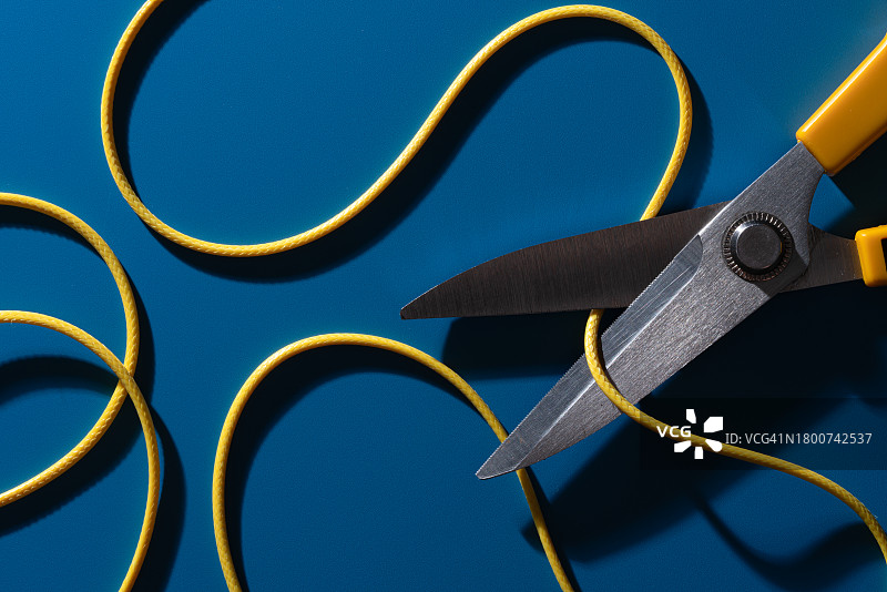 蓝色背景上剪刀切割弯曲的黄色电线图片素材