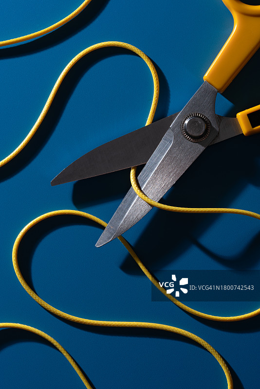 蓝色背景上剪刀切割弯曲的黄色电线图片素材