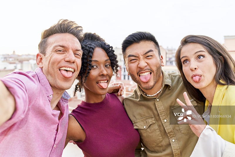 四个朋友拥抱、微笑并做着滑稽表情，看着镜头的自拍图片素材