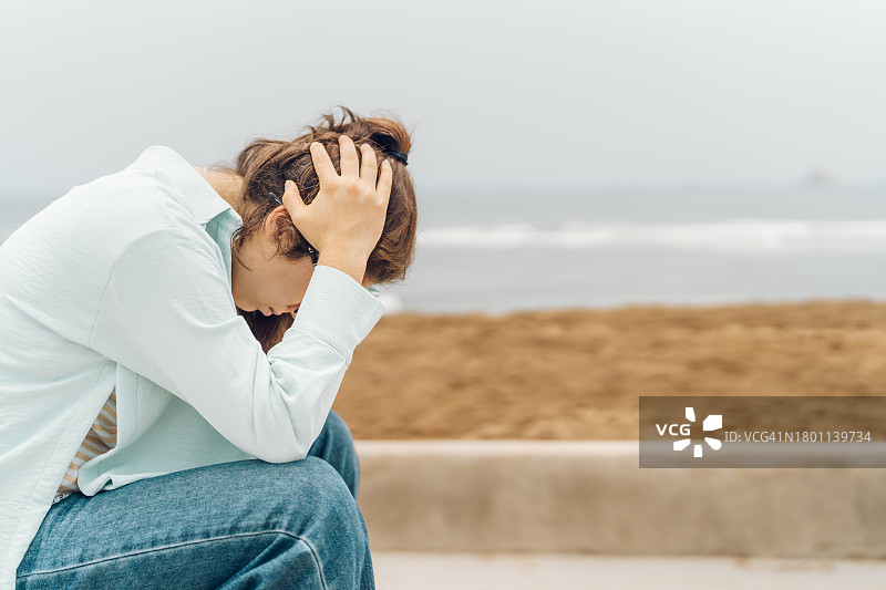 在海滩前抱着头的焦虑年轻女子图片素材